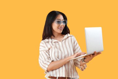 Sarı arka planda dizüstü bilgisayarla çalışan mutlu genç bayan Asyalı programcı.