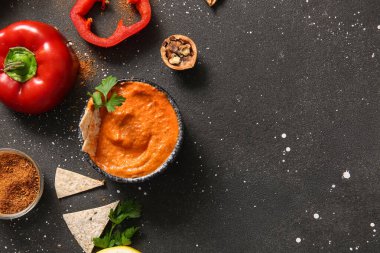 Bir kase lezzetli muhammara ve siyah arka planda malzemeler.