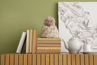 Kitaplar, çaydanlık ve fincanlar yeşil duvarın yanındaki ahşap dolapta, yakın plan.