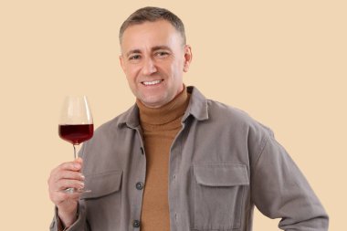 Bej arka planda bir bardak şarabı olan yakışıklı olgun bir adam.