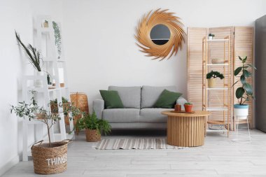 Oturma odasının içinde raf üniteleri, ev bitkileri, ayna, masa ve kanepe.