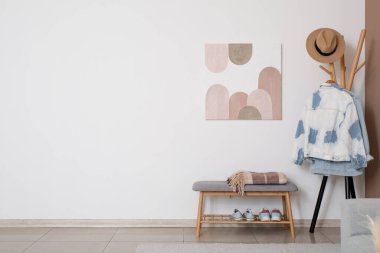 Beyaz duvarda gri banklar, askılık ve şık resimler asılı modern salonun içi.