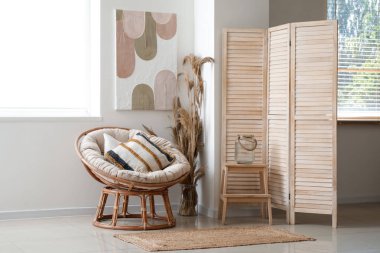 Modern oturma odasının içi rahat koltuğu, vazo dolusu çim, sehpa ve beyaz duvarda resmi olan.