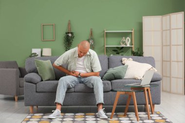 Apandisiti olan genç bir adam evdeki kanepede oturuyor.