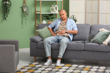 Apandisit ameliyatından sonra bandı olan genç bir adam evdeki kanepede oturuyor.