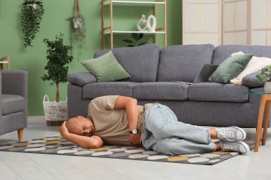 Evde yerde yatan apandisiti olan genç bir adam.