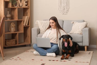 Tatlı Doberman köpeği ve evde dizüstü bilgisayarla çalışan genç ve güzel bir kadın.