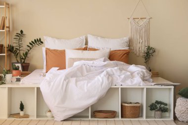 Büyük konforlu yatak, ev çiçekleri ve yatak odasının içindeki raf ünitesi.