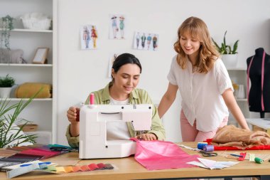 Atölyedeki masada kadın terziler dikiş dikiyor.