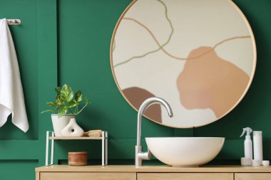 Modern lavabo, kavanoz ve kozmetik ürünleri banyodaki yeşil duvarın yanındaki dolapta.