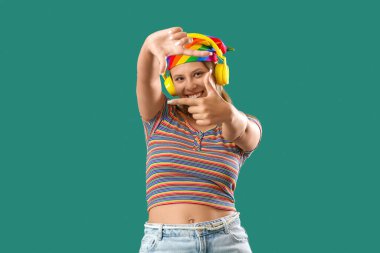 Kulaklıklı genç bir kadın yeşil arka planda çerçeve hareketi yapıyor.