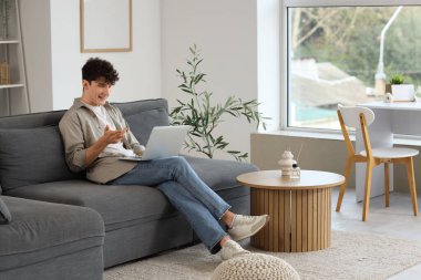 Genç adam evdeki kanepede dizüstü bilgisayarla görüntülü sohbet ediyor.