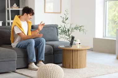 Genç adam evdeki kanepede dizüstü bilgisayarla görüntülü sohbet ediyor.