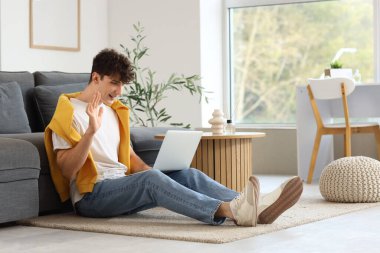 Genç adam evde dizüstü bilgisayarla görüntülü sohbet ediyor.