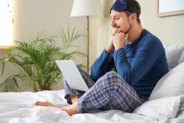 Evde yatağında dizüstü bilgisayarlı, pijamalı mutlu bir genç.