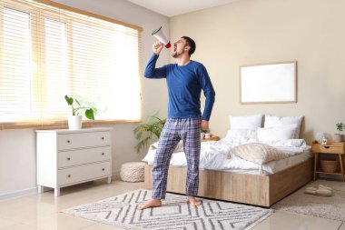 Pijamalı, megafonlu genç adam evde bağırıyor.