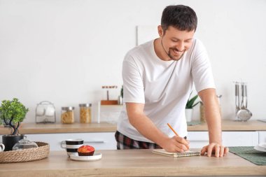 Evde pijamalı, defterli, kahveli ve kekli genç adam.