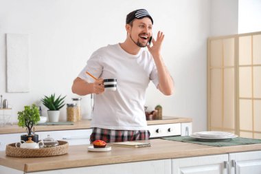 Evde pijamalı, pijamalı, kahveli ve kekli genç adam cep telefonuyla konuşuyor.