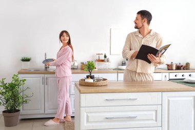 Kız arkadaşı evde bulaşık yıkarken genç adam dergi okuyor.