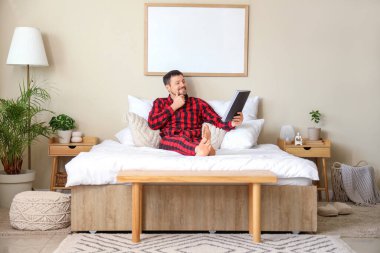 Evde yatağında dergileri olan damalı pijamalı mutlu genç bir adam.