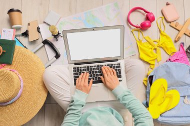 Zeminde plaj aksesuarları olan dizüstü bilgisayar kullanan kadın seyahat blogcusu.