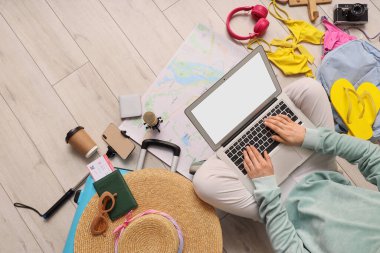 Zeminde plaj aksesuarları olan dizüstü bilgisayar kullanan kadın seyahat blogcusu.