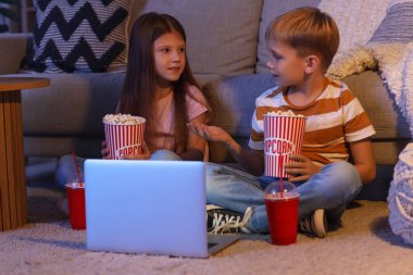 Küçük çocuklar ellerinde patlamış mısırla evde dizüstü bilgisayar seyrediyorlar.