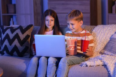 Küçük çocuklar ellerinde patlamış mısır ve sodayla evde dizüstü bilgisayar seyrediyorlar.