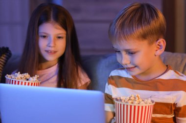 Küçük çocuklar ellerinde patlamış mısırla dizüstü bilgisayarlarında çizgi film izliyorlar.