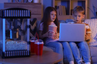 Şok olmuş küçük çocuklar evde dizüstü bilgisayar seyrediyor.