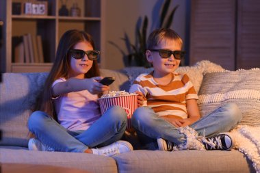Üç boyutlu gözlüklü ve patlamış mısırlı küçük çocuklar akşam evde TV 'de çizgi film izliyorlar.