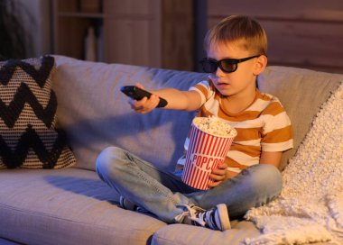 Üç boyutlu gözlüklü ve patlamış mısırlı küçük çocuk akşam evde TV 'de çizgi film izliyor.