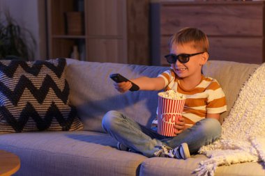 Üç boyutlu gözlüklü ve patlamış mısırlı küçük çocuk akşam evde TV 'de çizgi film izliyor.