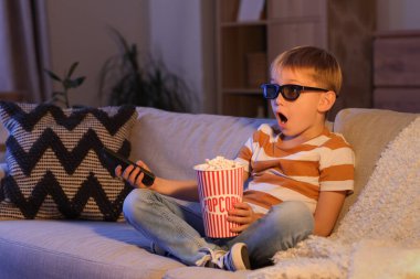 Şok olmuş üç boyutlu gözlüklü ve patlamış mısırlı küçük çocuk akşam TV 'de film izliyor.