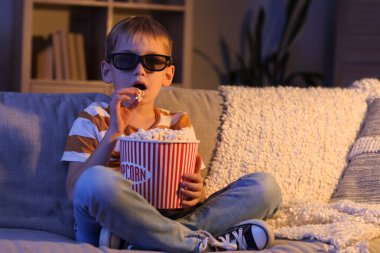 Üç boyutlu gözlüklü ve patlamış mısırlı küçük çocuk akşam evde film izliyor.