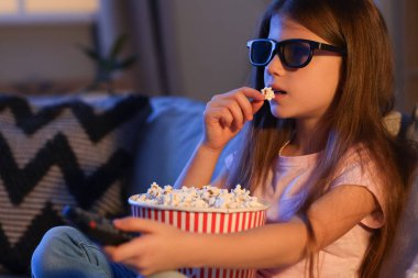 Üç boyutlu gözlüklü ve patlamış mısırlı küçük kız akşam evde film izliyor, yakın plan.