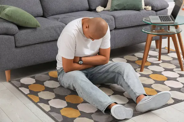 Apandisiti olan genç bir adam evde yerde oturuyor.