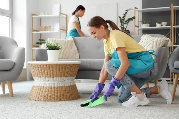 Kadın hademe odada halı süpürüyor.