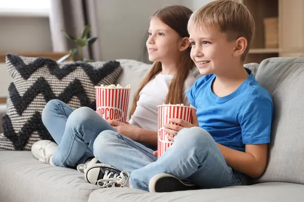 Küçük çocuklar ellerinde patlamış mısırla evdeki kanepede film izliyorlar.