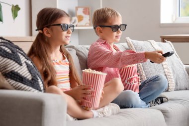 Üç boyutlu gözlüklü, patlamış mısırlı küçük çocuklar evde televizyon seyrediyor.