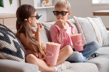 Üç boyutlu gözlüklü, patlamış mısırlı küçük çocuklar evdeki kanepede film izliyorlar.