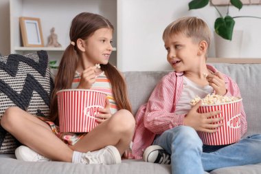 Küçük çocuklar ellerinde patlamış mısırla evdeki kanepede film izliyorlar.