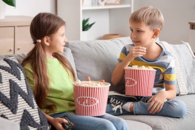 Küçük çocuklar ellerinde patlamış mısırla evdeki kanepede film izliyorlar.