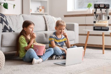 Patlamış mısırlı küçük çocuklar evde dizüstü bilgisayardan film izliyorlar.