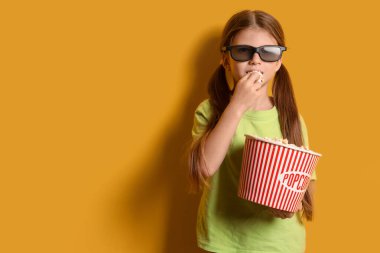 Üç boyutlu gözlüklü küçük kız sarı arka planda patlamış mısır yiyor.