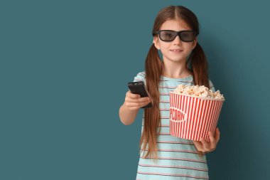 Üç boyutlu gözlüklü, patlamış mısırlı küçük kız mavi arka planda televizyon izliyor.