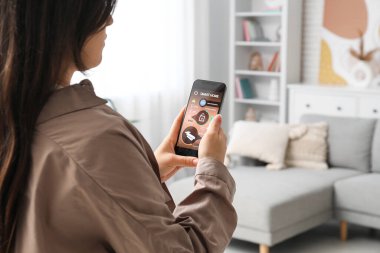 Akıllı ev güvenlik sistemi uygulaması olan cep telefonu kullanan genç bir kadın.