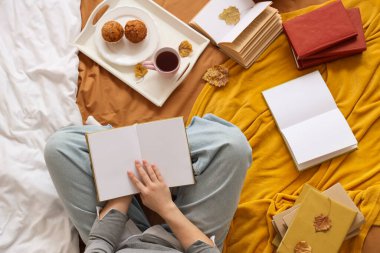 Tepsi ve sonbahar yapraklarıyla kitap okuyan bir kadın.