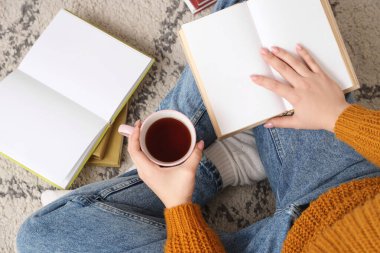 Kahve fincanı ve boş kitapları olan kadın halıda oturuyor.