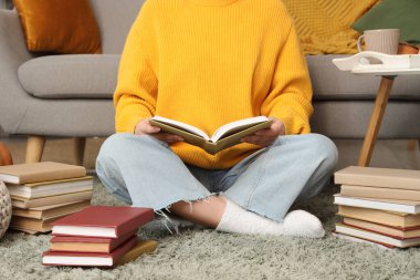 Evde halıda kitap okuyan bir kadın.